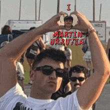a man making a heart shape with his hands with the name martin urrutia written on it
