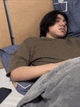 a man laying on a bed with his eyes closed and a grey blanket