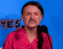 a man in a red shirt stands in front of a microphone with the word yes written on the wall behind him