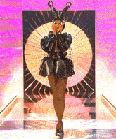 a drag queen is standing on a stage wearing a black dress and a hat with horns .
