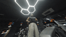 a man stands in a gym holding a dumbbell under a hexagonal ceiling