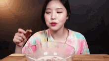 a young woman is eating a piece of food from a bowl .
