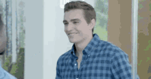a man in a blue plaid shirt is smiling while standing next to another man .