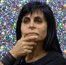 a woman with long black hair is thinking with her hand on her chin .