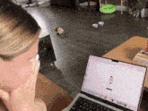 a woman is sitting in front of a laptop with a cartoon character on the screen