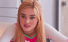a young woman with blonde hair and blue eyes is wearing a pink and green outfit and looking at the camera .