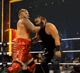 two men are wrestling in a wrestling ring and one of them is wearing red shorts .