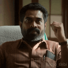 a man with a beard is sitting in a chair and the name sanjo_sebi is on the bottom