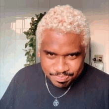 a man with blonde hair and a mustache is wearing a black shirt and a necklace with a pentagram pendant .