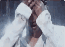 a man in a white shirt is covering his face with his hands while crying .