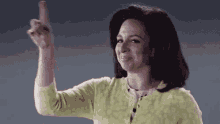 a woman in a green sweater is pointing her finger up .
