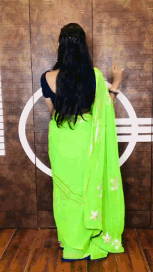 a woman wearing a neon green saree is standing in front of a wooden wall