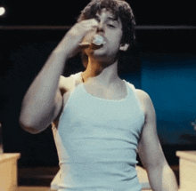 a man wearing a white tank top is drinking from a bottle