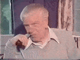 an older man is talking on a cell phone while sitting in a chair .