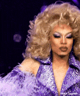 a drag queen is wearing a purple dress with feathers and a wig .