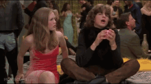 a woman in a red dress sits next to a man in a black turtleneck in a movie scene from movieclips.com