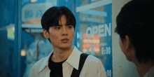 a man and a woman are standing in front of a store window that says open