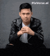 a man in a black leather jacket is sitting with his hands folded in front of a pixverse.ai logo