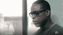 a man wearing glasses and a gray sweater is looking out a window .