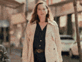 a woman in a trench coat is walking down a city street