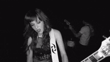 a woman is playing a guitar in a black and white photo while a man plays drums in the background .