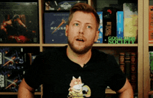 a man wearing a black shirt with a fox on it stands in front of a shelf full of games