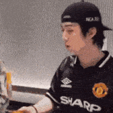 a man wearing a baseball cap and a sharp jersey is sitting at a table eating food .
