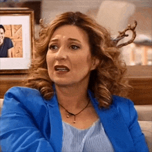 a woman wearing a blue jacket and a necklace is sitting on a couch