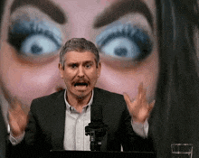 a man in a suit is speaking into a microphone in front of a woman 's face