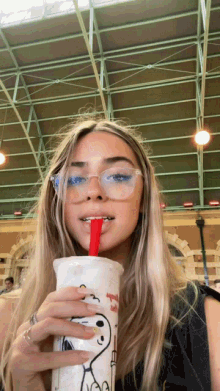 a woman with glasses is drinking from a snoopy cup