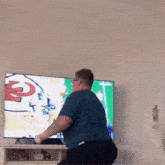 a man in a blue shirt is dancing in front of a flat screen tv with the letter t on it