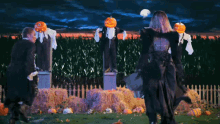 a couple of people dancing in front of scarecrows that have pumpkins on their heads