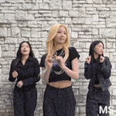 three women are dancing in front of a brick wall with ms written on the bottom