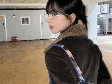 a woman wearing glasses and a brown jacket is standing in a room