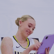 a woman in a basketball uniform is holding a purple tablet in her hands .