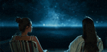 two women are sitting in lawn chairs looking at the night sky