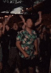 a man in a hawaiian shirt is dancing in a crowd .