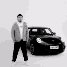 a black and white photo of a man standing in front of a mini cooper with a license plate that says pandas