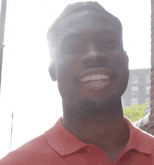 a man in a red shirt is smiling and looking at the camera while standing in front of a building .