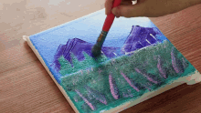 a person is painting a landscape with a brush on a canvas