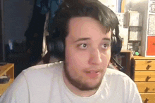 a man with a beard wearing headphones and a white shirt is looking at the camera .