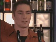 a man stands in front of a shelf of alcohol bottles including one that says ' 4 ' on it