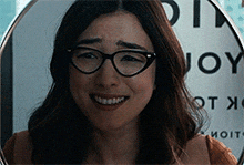 a woman wearing glasses is smiling in front of a sign that says joy on it