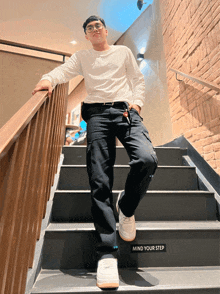 a man leans against a railing on a set of stairs with a sign that says mind your step