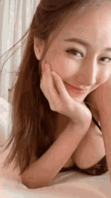 a woman in a bra is laying on a bed with her hand on her face and smiling .