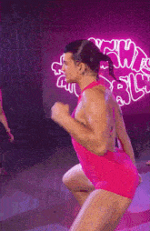 a man in a pink bodysuit is dancing in front of a neon sign that says rc