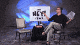 a man sits in front of a sign that says hey ew