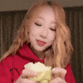 a woman in a red hoodie is eating a piece of bread .