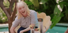 a woman is sitting on a wicker chair next to a pool laughing .