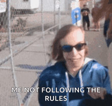 a blurry picture of a woman wearing sunglasses and a blue hoodie that says me not following the rules